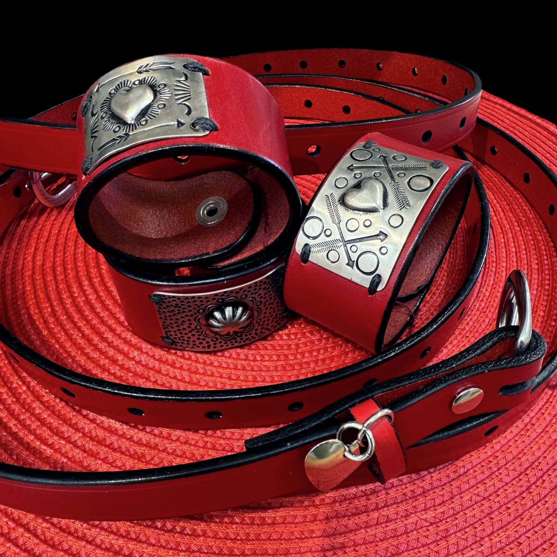 Red leather cuffs and belts with stamped silver conchos, by Diane Louise Paul
